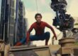 Tom Holland vestido como Homem-Aranha agachado sobre um veículo militar durante as filmagens de uma cena de ação, com um equipamento de câmera suspenso ao lado capturando a cena. Ao fundo, é possível ver prédios modernos e o céu parcialmente nublado