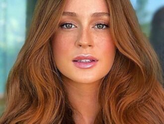 A imagem mostra um retrato da atriz e modelo Marina Ruy Barbosa. Ela tem cabelos ruivos longos e ondulados, e está olhando diretamente para a câmera com um olhar intenso e expressivo. O fundo é desfocado, deixando o foco principal na face de Marina. Ela parece estar usando uma maquiagem natural, com destaque para seus olhos e lábios. A iluminação suave e a composição da imagem criam um efeito elegante e sofisticado, realçando a beleza e o carisma da atriz