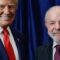 A imagem registra um momento diplomático entre os presidentes Donald Trump, dos Estados Unidos, e Luiz Inácio Lula da Silva, do Brasil. Ambos aparecem em frente a uma cortina azul escura, sorrindo e apertando as mãos em gesto de cordialidade. Trump veste um terno azul com camisa branca e gravata vermelha, enquanto Lula usa um terno escuro com camisa azul clara e gravata vinho.