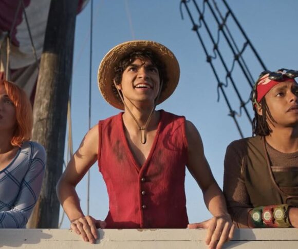 A direita três pessoas olham para o horizonte dentro de um barco
