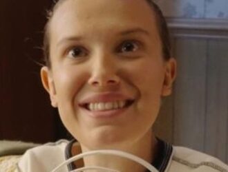 Millie Bobby Brown sorri enquanto segura um dos aparatos que sua personagem Eleven usou na primeira temporada da série