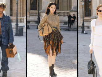 A imagem mostra três personalidades em looks de street style durante um evento de moda. À esquerda, um homem usa conjunto oversized de jeans escuro, sem camisa por baixo, carregando uma maleta de madeira. No centro, uma mulher veste blusa dourada de tricô com saia assimétrica de estampa xadrez, combinada com bota preta e bolsa estruturada. À direita, outra mulher aparece com um vestido longo off-white ajustado, de mangas bufantes, completando o visual com óculos escuros e bolsa preta