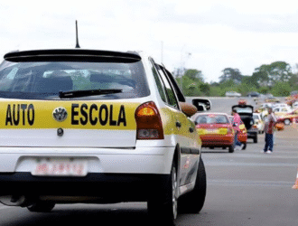 Carro de autoescola em local de treinamento com outros veículos ao redor e sinalizações de trânsito