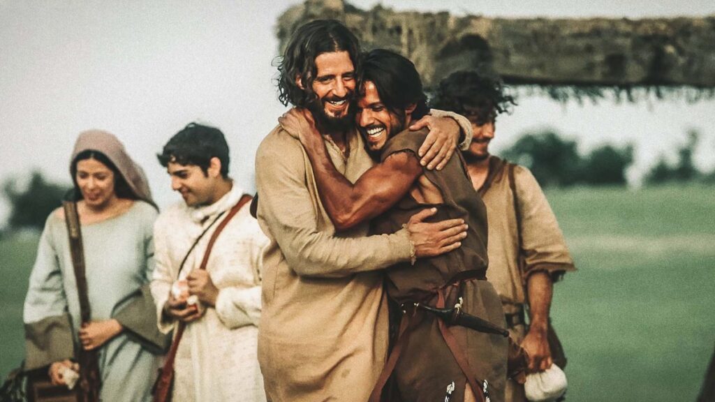 The Chosen no Guinness Book. Imagem mostra dois atores em primeiro plano: homens, cabelos escuros, roupas de época, se abraçam enquanto caminham. Ao fundo, uma mulher e outro homem aparecem, ambos com cabelos escuros e roupas de época. 