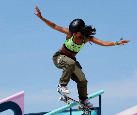 Imagem exibe uma jovem em uma manobra de skate