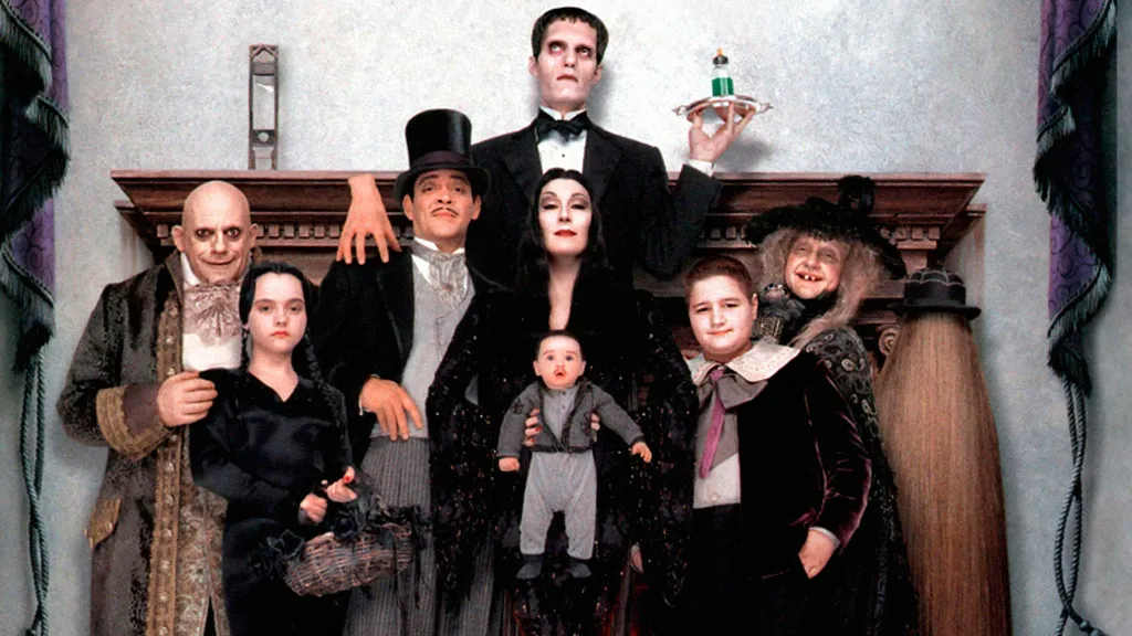 A imagem mostra toda a família Addams reunida. Todos vestem roupas pretas, no geral aveludadas, e exibem um rosto sério, digno da expressão da clássica família. Eles estão em frente possivelmente de uma lareira, num ambiente acinzentado.