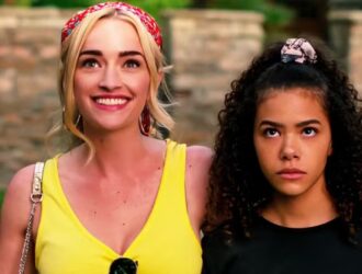 Na imagem, aparecem as personagens Georgia Miller, interpretada por Brianne Howey, e Ginny Miller, vivida por Antonia Gentry, da série "Ginny & Georgia". Georgia está sorridente, vestindo uma blusa amarela e uma faixa vermelha no cabelo, com o braço sobre o ombro da filha. Ao lado, Ginny exibe uma expressão séria e pensativa, usando uma blusa escura e um penteado com scrunchie. A cena simboliza o contraste entre a personalidade expansiva da mãe e a introspecção da filha, um dos eixos centrais da trama