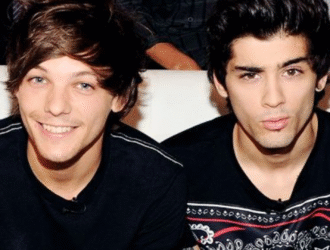 Louis Tomlinson e Zayn Malik, ex-integrantes da banda One Direction, posam juntos em um sofá. Louis sorri e mostra sinal de positivo com a mão, enquanto Zayn faz uma expressão descontraída com os lábios levemente franzidos. Ambos usam camisetas escuras, revelando parte de suas tatuagens nos braços